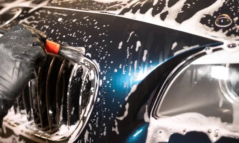 homme nettoyant le pare-choc d'une voiture au pinceau